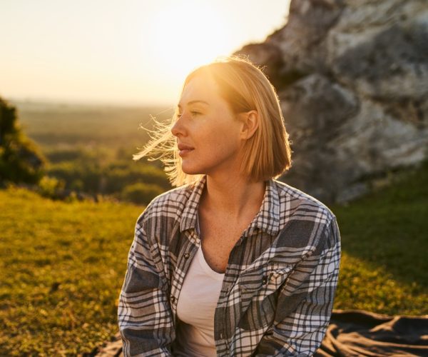 Thoughtful,Woman,Sitting,On,Hillside,At,Golden,Hour,Sunset,With